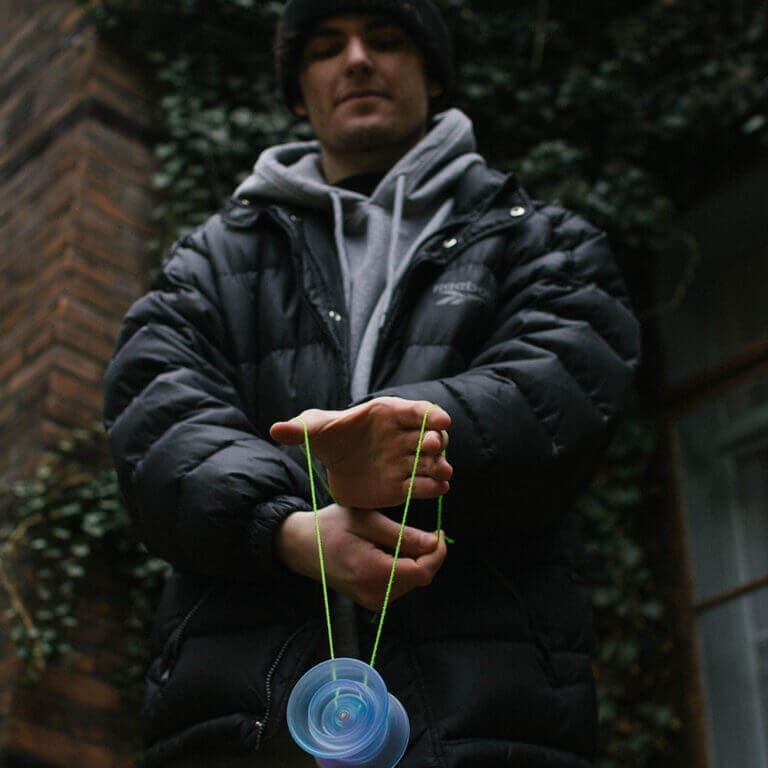 Young man demonstrating advanced yo-yo tricks outdoors with a vibrant green string.